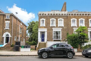 A black SUV parked in front of a row of terraced houses with brick facades and white window frames. - Spacious & stylish 2 bedroom apartment in Kentish Town (London)