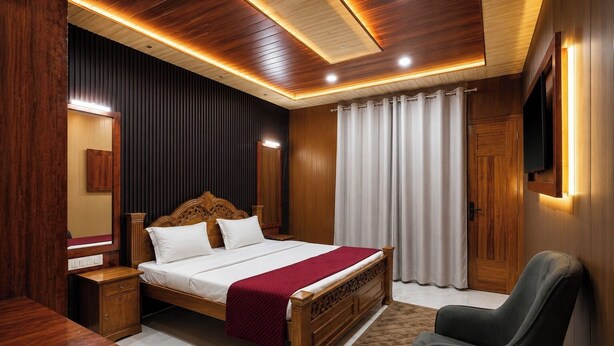 A hotel room with a wooden bed, a desk, a chair, a television, and a large window with curtains. - The Gautam Resort (Varanasi)