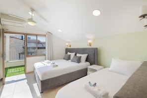 Una habitación de hotel con cama, mesita de noche, ventilador de techo y vistas al exterior.
