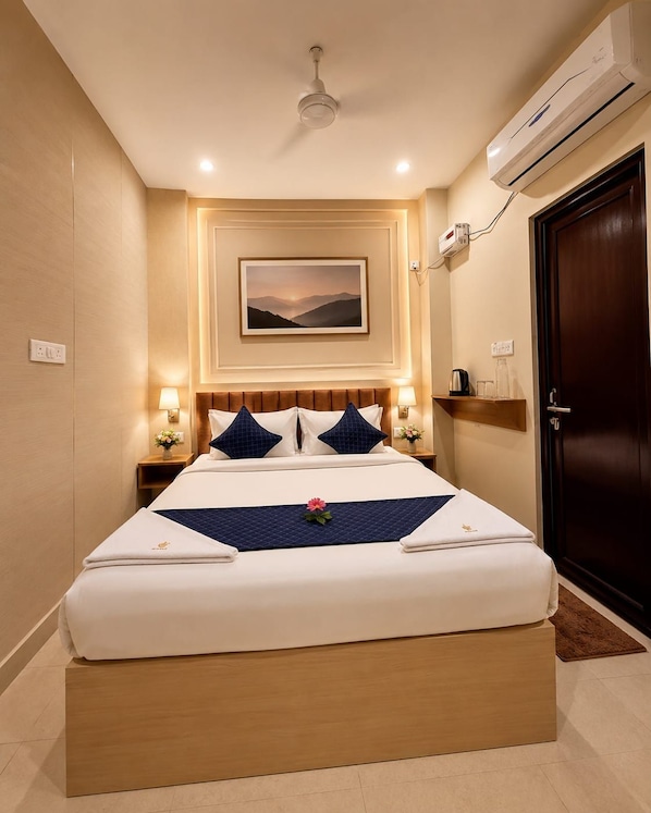 A hotel room with a bed, bedside lamps, a wall-mounted air conditioner, a framed picture, and a door.