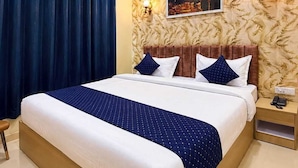 A hotel room with a large bed, a ceiling fan, a nightstand with a phone, and a wall-mounted light fixture. - Hotel Tapovan Inn (Varanasi)