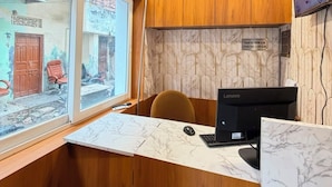 A room with a wooden ceiling, a ceiling fan, a desk with a computer, and a window overlooking a street. - Hotel Tapovan Inn (Varanasi)