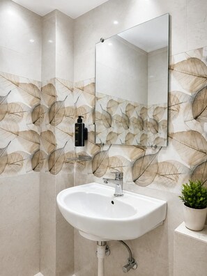 A bathroom with a white sink, a mirror, and a wall with a leaf pattern. - Hotel Tapovan Inn (Varanasi)