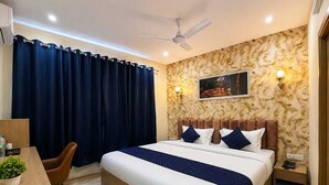 A hotel room with a bed, a desk, a chair, a ceiling fan, and a wall-mounted TV. - Hotel Tapovan Inn (Varanasi)