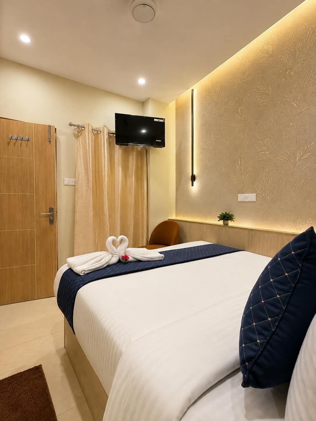 Habitació d'hotel amb un llit, un televisor fixat a la paret, una porta de fusta i una cortina.