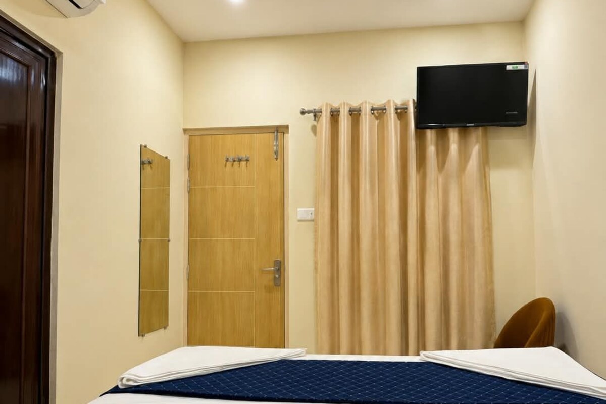 A hotel room with a bed, a television mounted on the wall, a door, and a curtain.