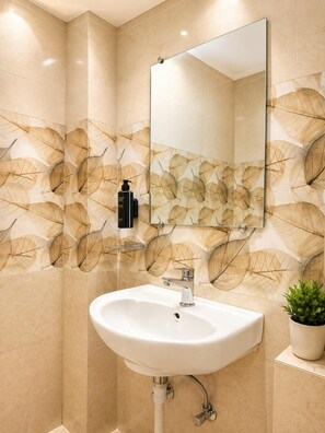 Un baño con un lavamanos blanco, un espejo y una pared con diseño de hojas.
