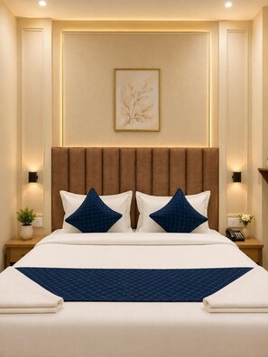 A hotel room with a large bed, two bedside tables, a wall-mounted artwork, and a nightstand with a phone and a plant. - Hotel Tapovan Inn (Varanasi)