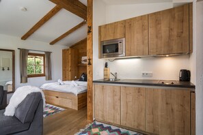 Ein kleines Zimmer mit einem Bett, einer kompakten Küchenzeile mit Holzschränken, einer Mikrowelle und einem Spülbecken.