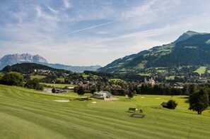 Ein Golfplatz mit Clubhaus, Teich und einem Bergpanorama im Hintergrund.
