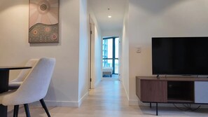 Una moderna camera d'albergo con televisione a schermo piatto, una sedia bianca e un corridoio che conduce a un balcone con vista.