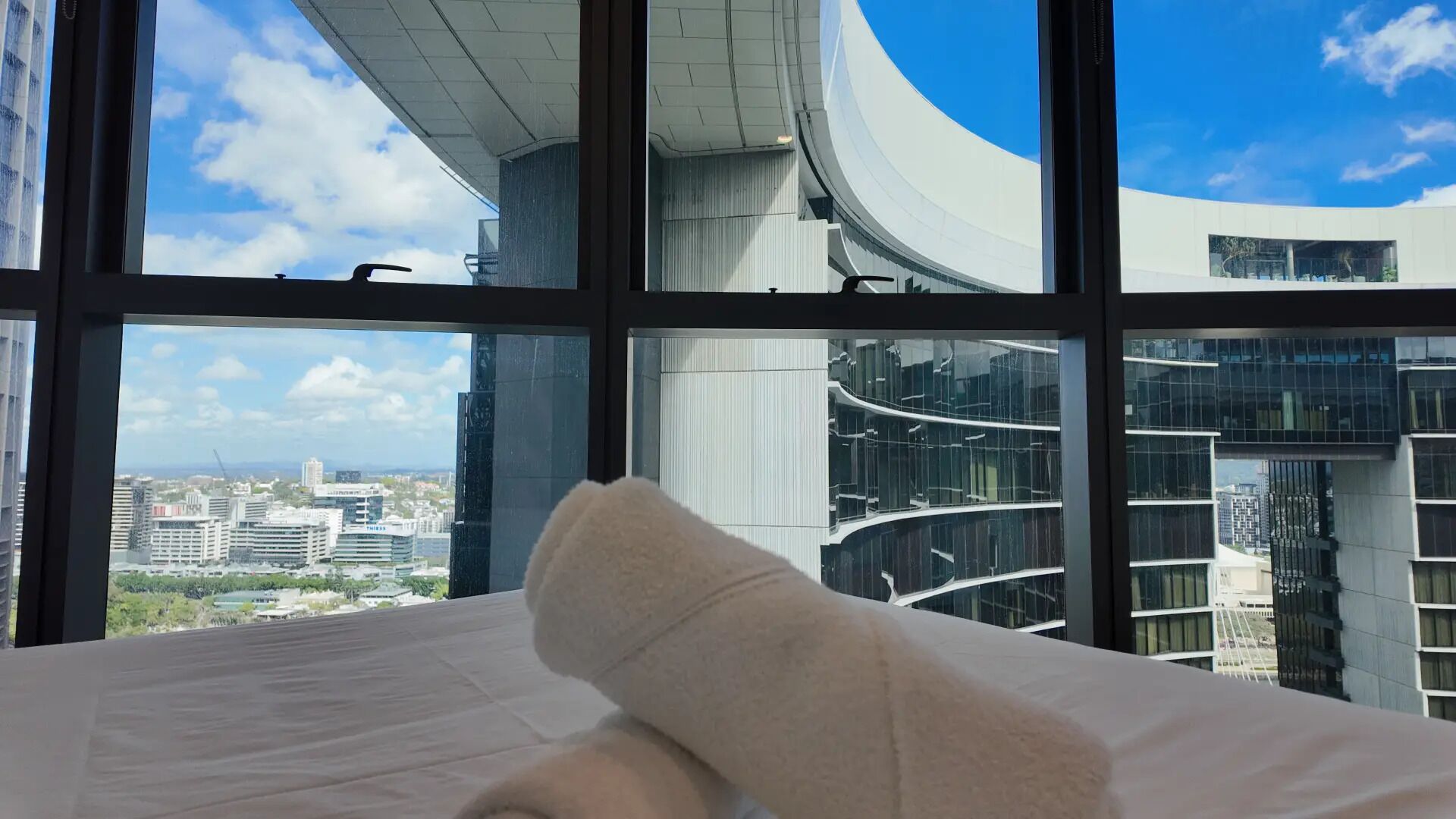 Cama com vista para um edifício moderno e arquitetura curvilínea, sob um céu claro.