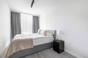 A modern bedroom with a bed, curtains, a nightstand, and a lamp. - Comfortable Apartment with Parking Space | 2 Bedrooms | City Centre (Lublin)