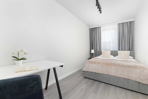 A modern bedroom with a bed, a bedside table with a book and flowers, and a desk with a chair. - Comfortable Apartment with Parking Space | 2 Bedrooms | City Centre (Lublin)