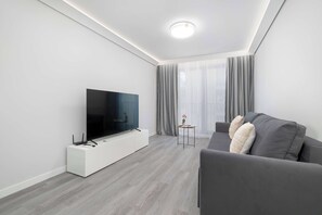 A modern living room with a flat-screen TV, grey sofa, and a small side table. - Comfortable Apartment with Parking Space | 2 Bedrooms | City Centre (Lublin)