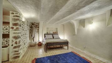 A bedroom with a stone wall, a bed with patterned bedding, a blue rug, and a tiled floor.