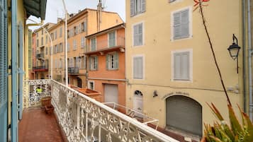 A balcony with ornate white railings, adjacent buildings with shutters, and a potted plant.