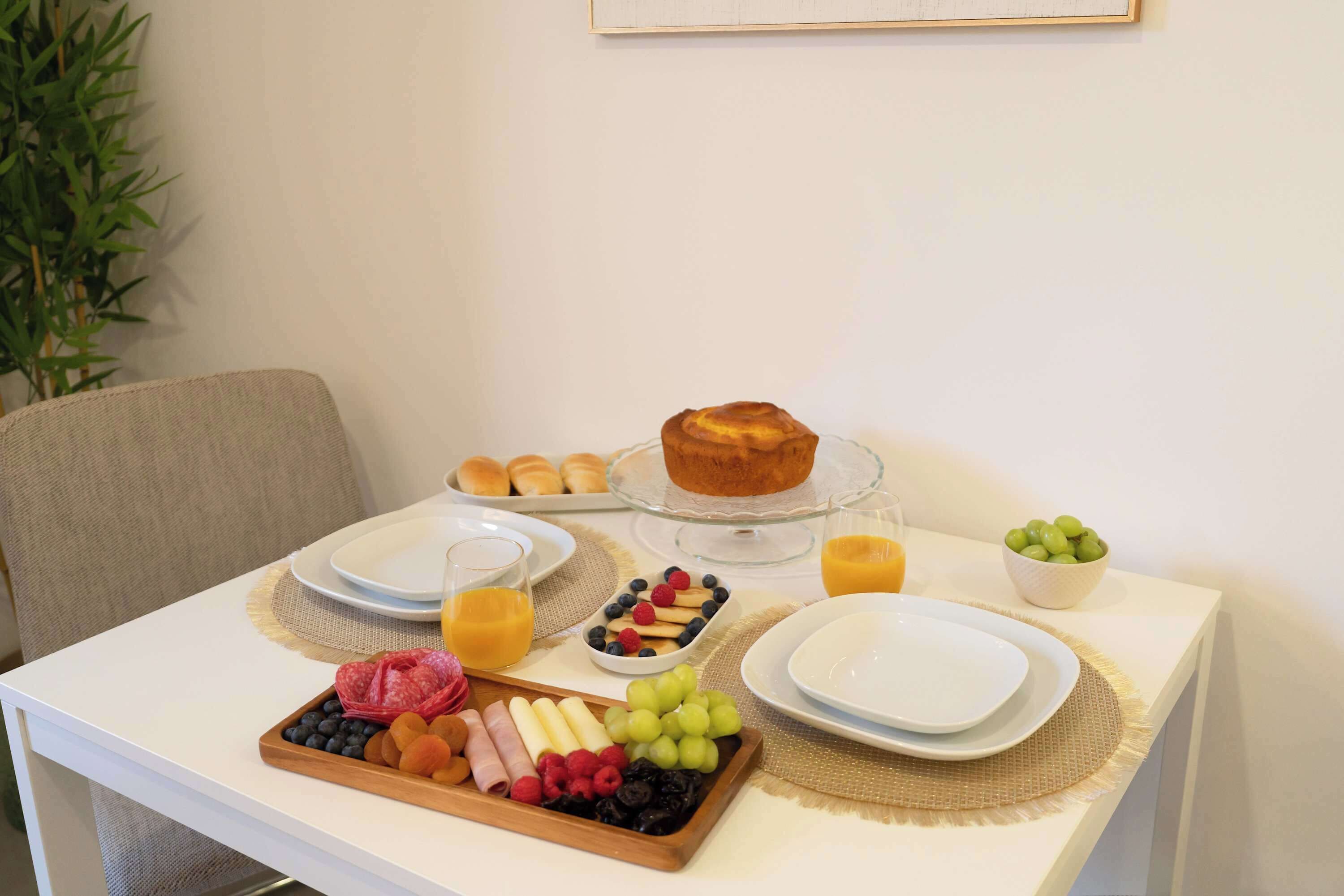 A breakfast table with a variety of food items, including a plate of pastries, a glass of orange juice, and a fruit platter.