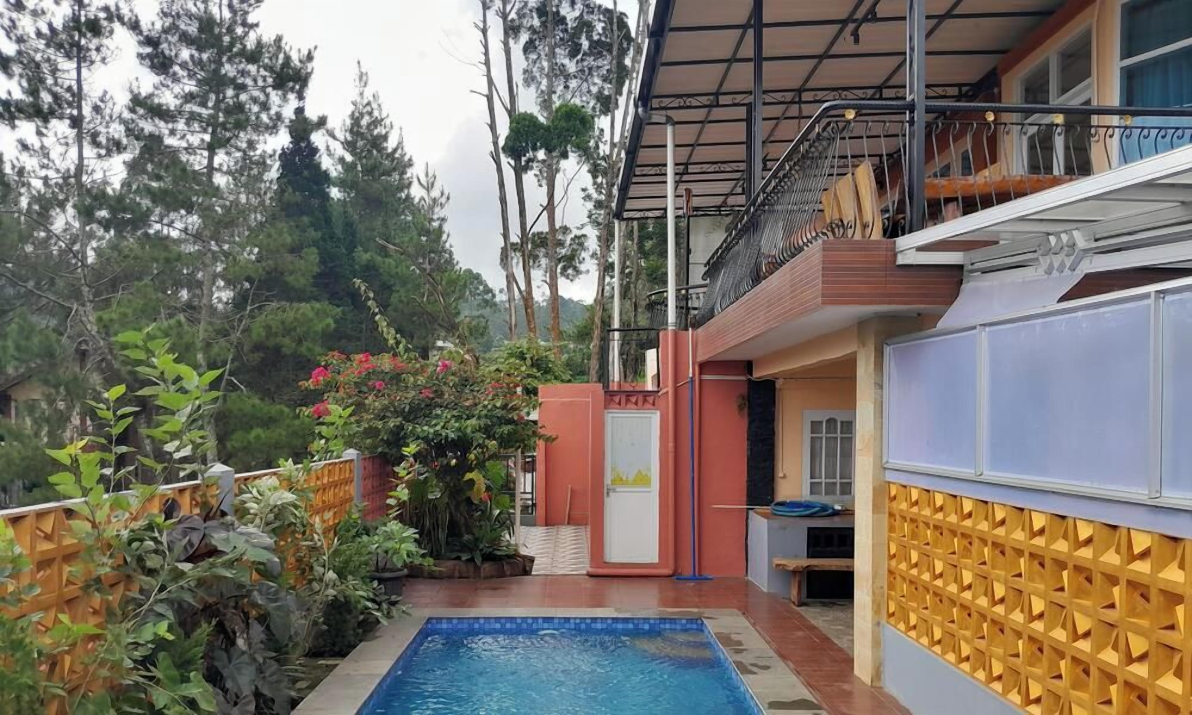 Zona de piscina con terraza de madera, un espacio de estar cubierto y vista a un área boscosa.