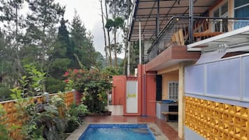 Zona de piscina con terraza de madera, un espacio de estar cubierto y vista a un área boscosa.
