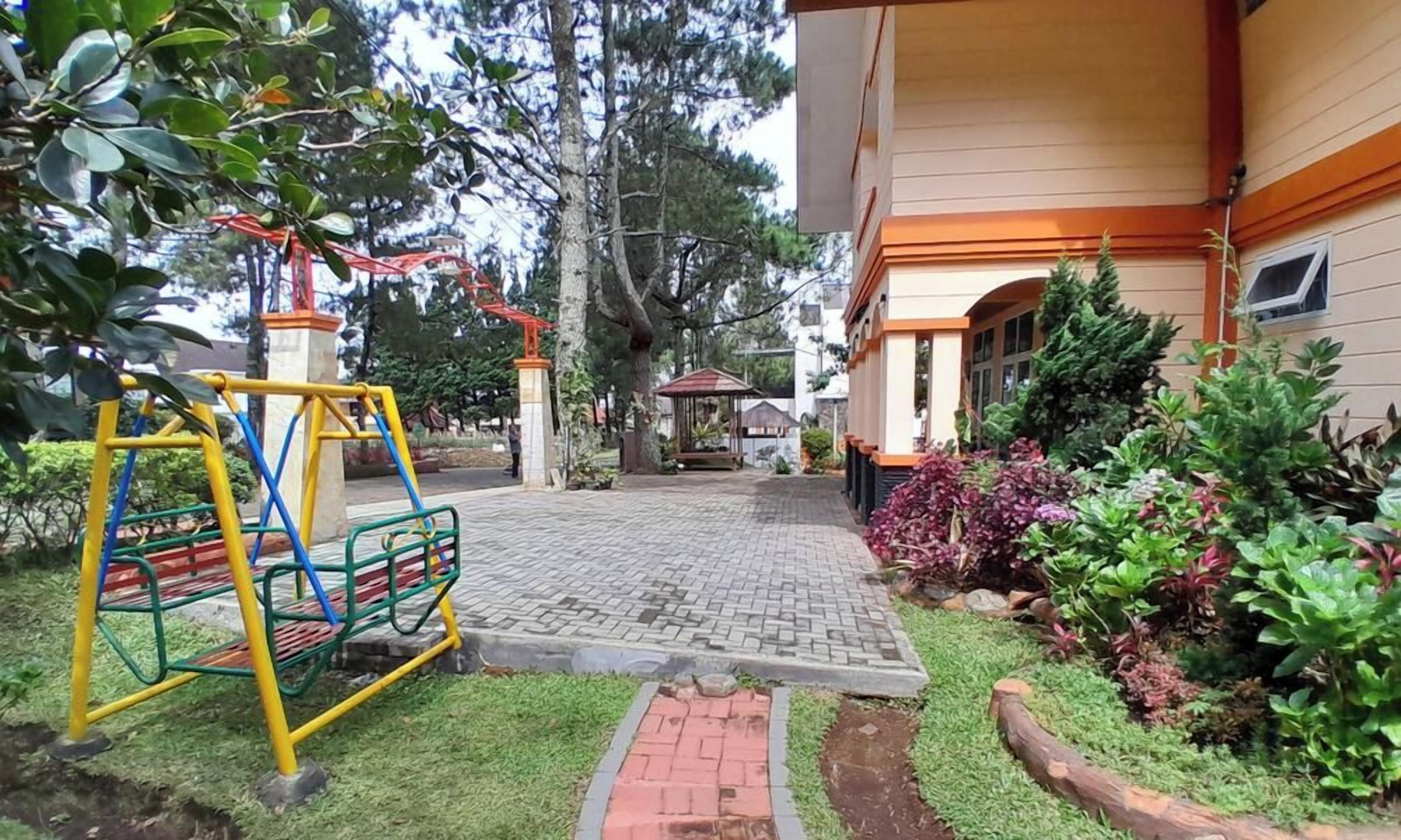 A playground with swings and a slide, a paved pathway, and a building with a covered entrance.