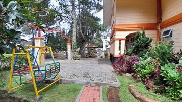 A playground with swings and a slide, a paved pathway, and a building with a covered entrance.