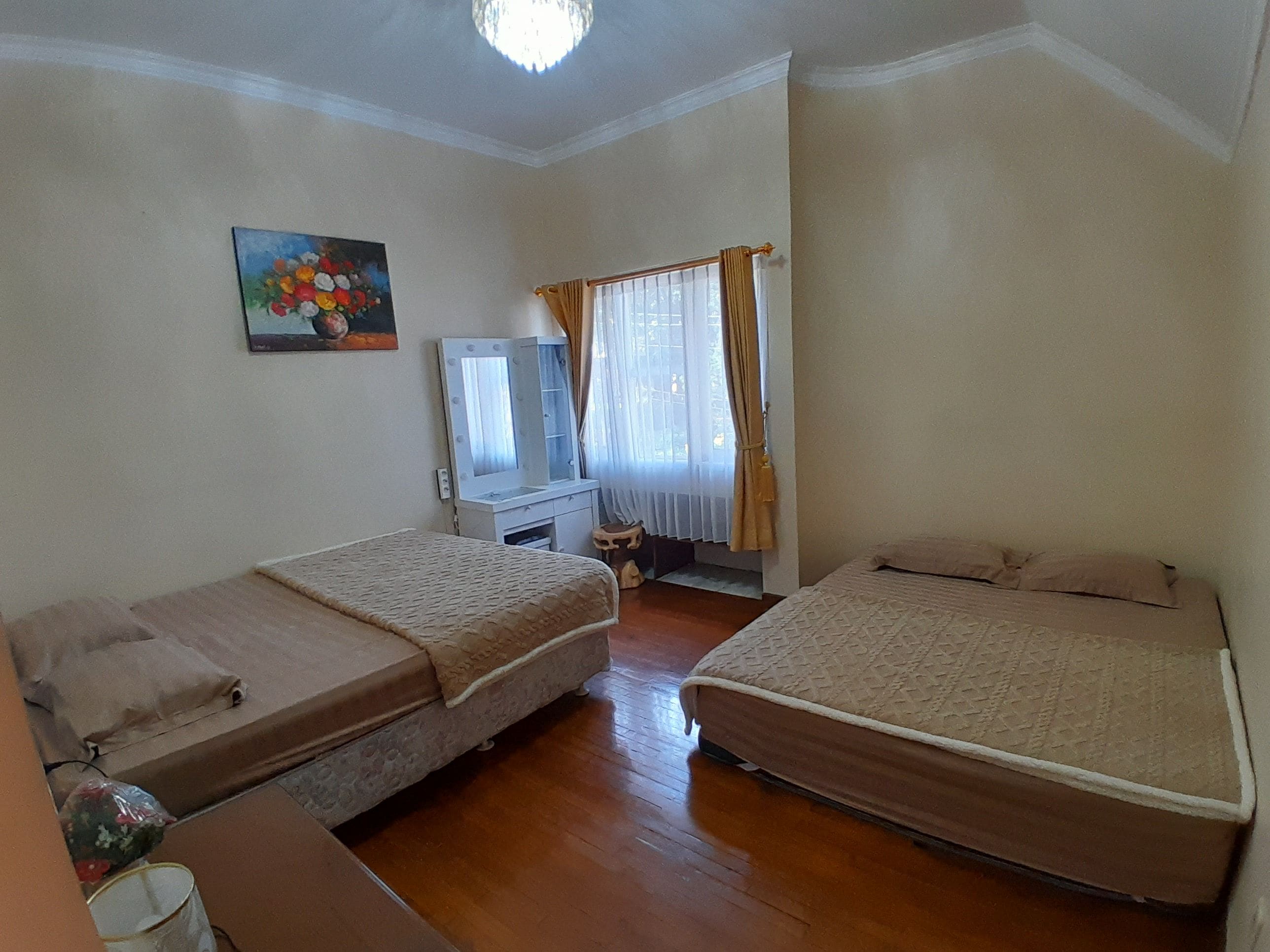 Una habitación con dos camas, un tocador con espejo, un cuadro en la pared y una ventana con cortinas.