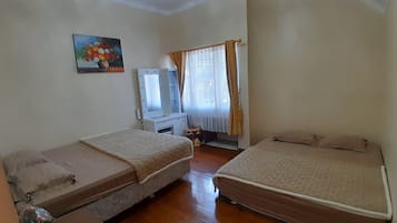 Una habitación con dos camas, un tocador con espejo, un cuadro en la pared y una ventana con cortinas.