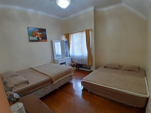 Una habitación con dos camas, un tocador con espejo, un cuadro en la pared y una ventana con cortinas.