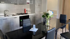 A modern kitchen with grey cabinets, a stainless steel sink, and a glass dining table with black chairs.