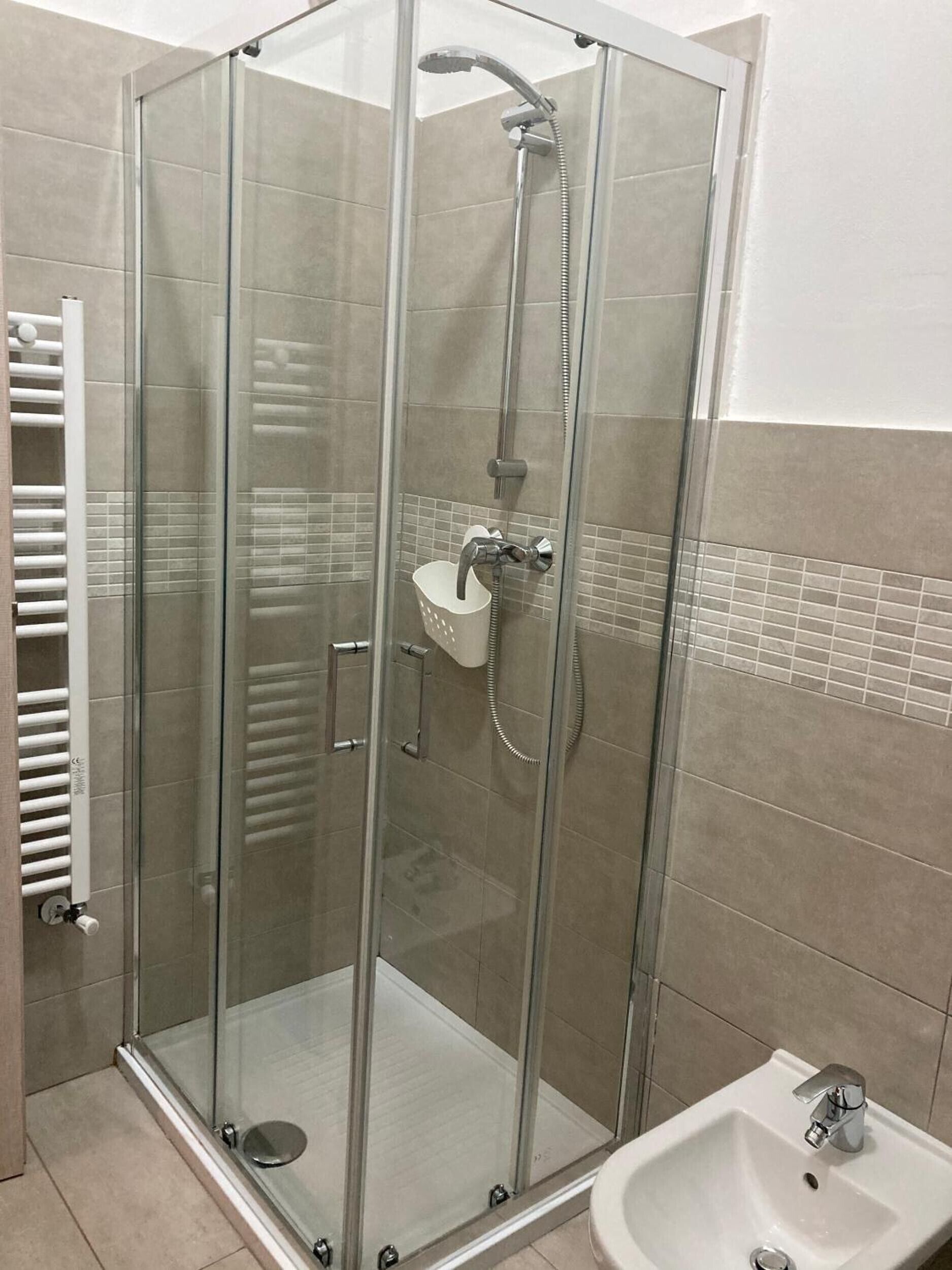 Een douchecabine met glazen wanden, een handdouche en een kraan op de muur.