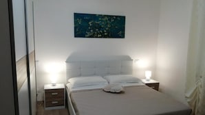 A bedroom with a large bed, two bedside tables, a nightstand, and a wall-mounted painting.