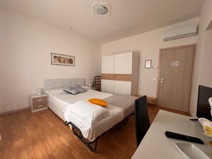 Ein Schlafzimmer mit Bett, Nachttischen, einem Schreibtisch, einer Klimaanlage und einer Tür.
