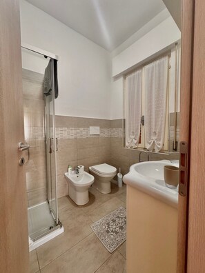 A modern bathroom with a glass shower enclosure, a bidet, a toilet, and a bathtub.