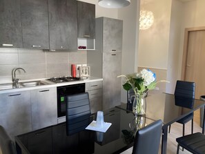 A modern kitchen with grey cabinets, a stainless steel sink, and a glass dining table with black chairs.