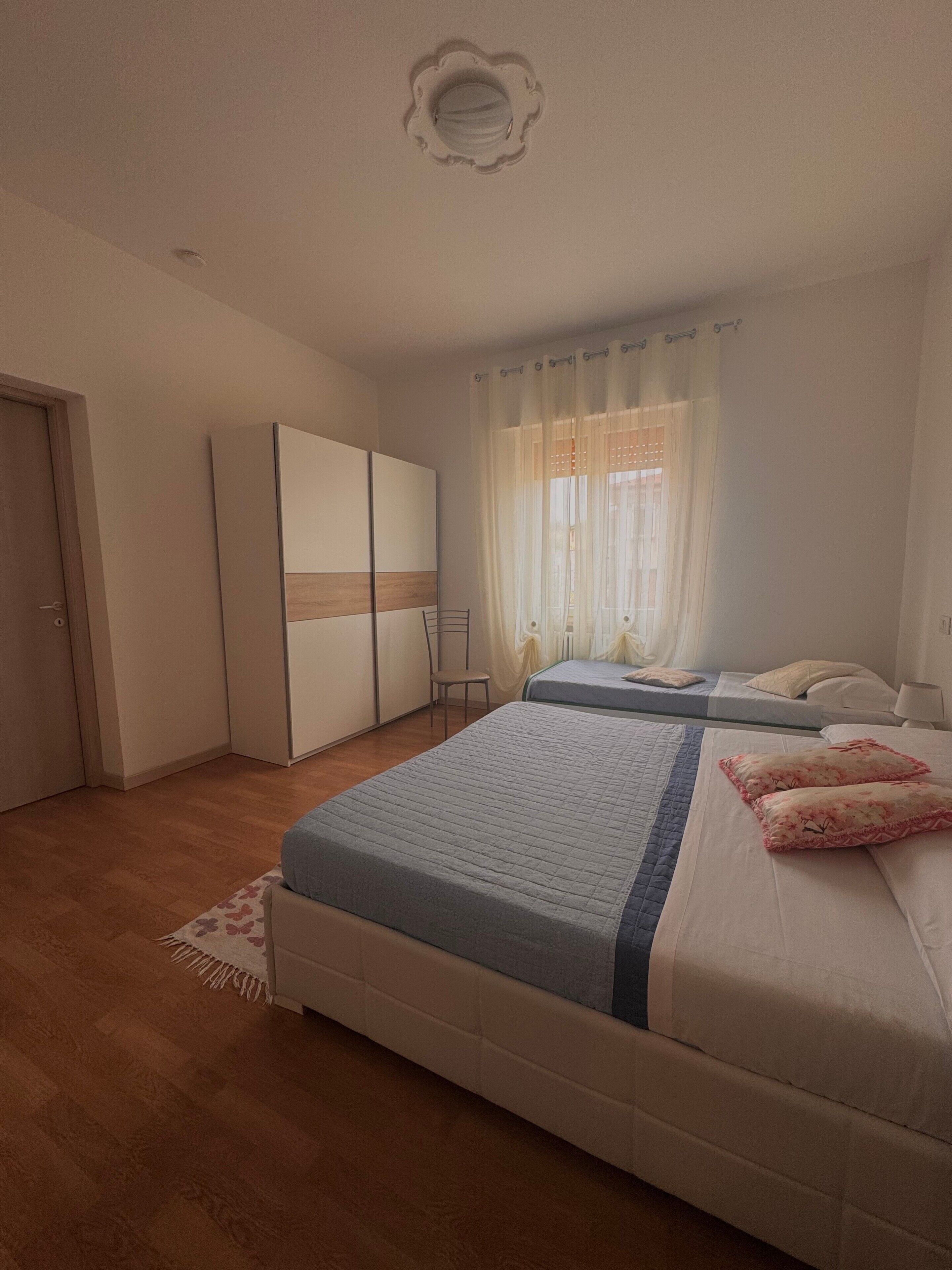 Une chambre à coucher avec un lit, une armoire, une chaise et une fenêtre avec des rideaux.