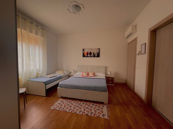 A bedroom with two beds, a wooden floor, a painting on the wall, and a door on the right.