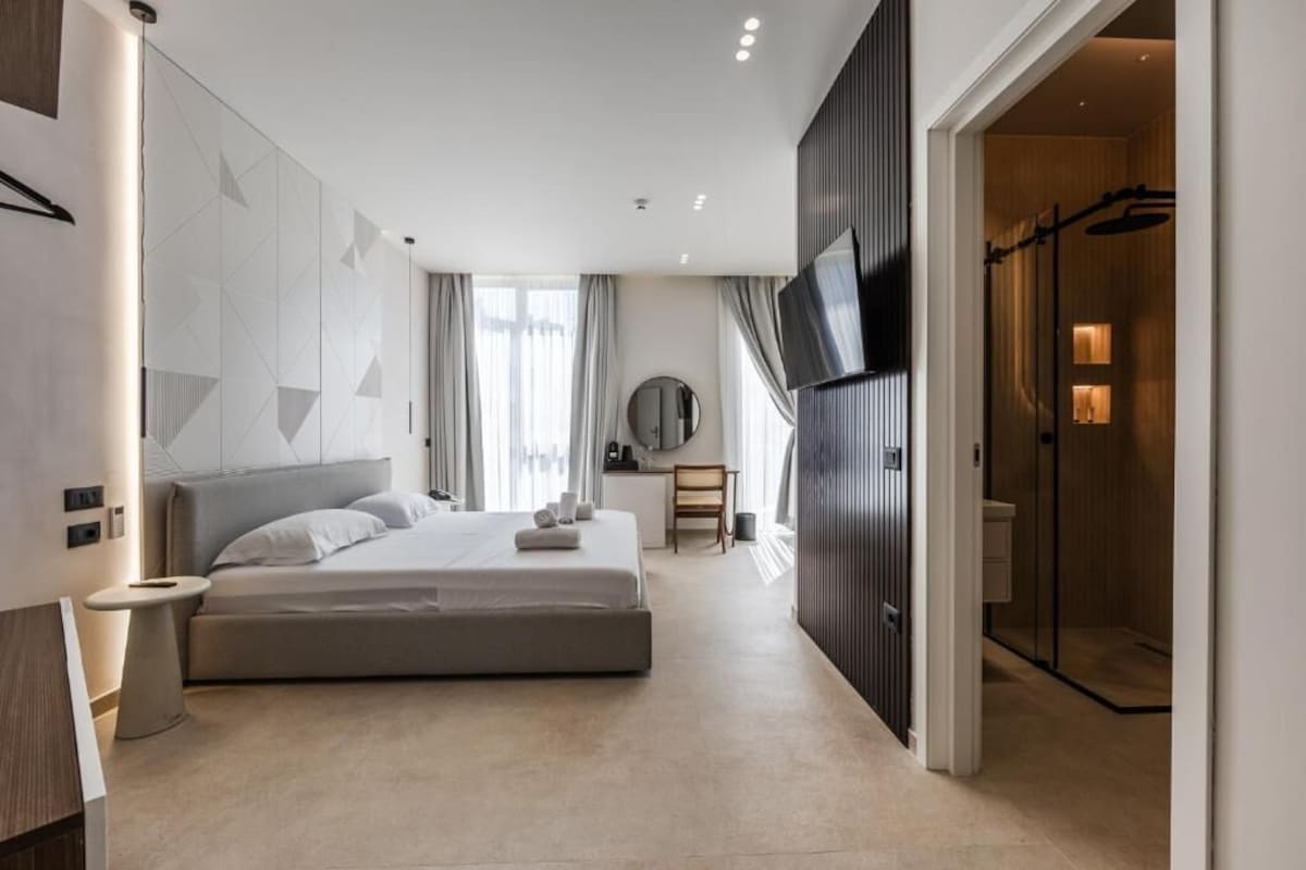 Ein modernes Hotelzimmer mit einem großen Bett, einem Fernseher, einem Schreibtisch und einem begehbaren Kleiderschrank.