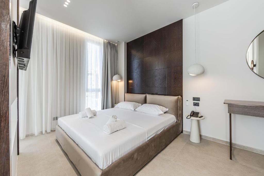 Ein modernes Hotelzimmer mit einem großen Bett, einem Nachttisch, einem Spiegel und einem an der Wand befestigten Fernseher.