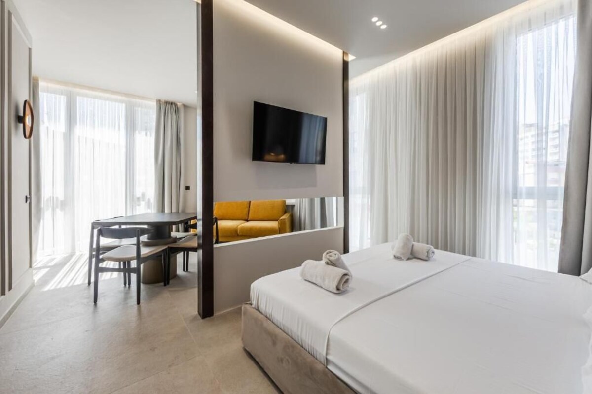 Ein Hotelzimmer mit Bett, Schreibtisch, Stuhl, Wandfernseher und großem Fenster mit Vorhängen.