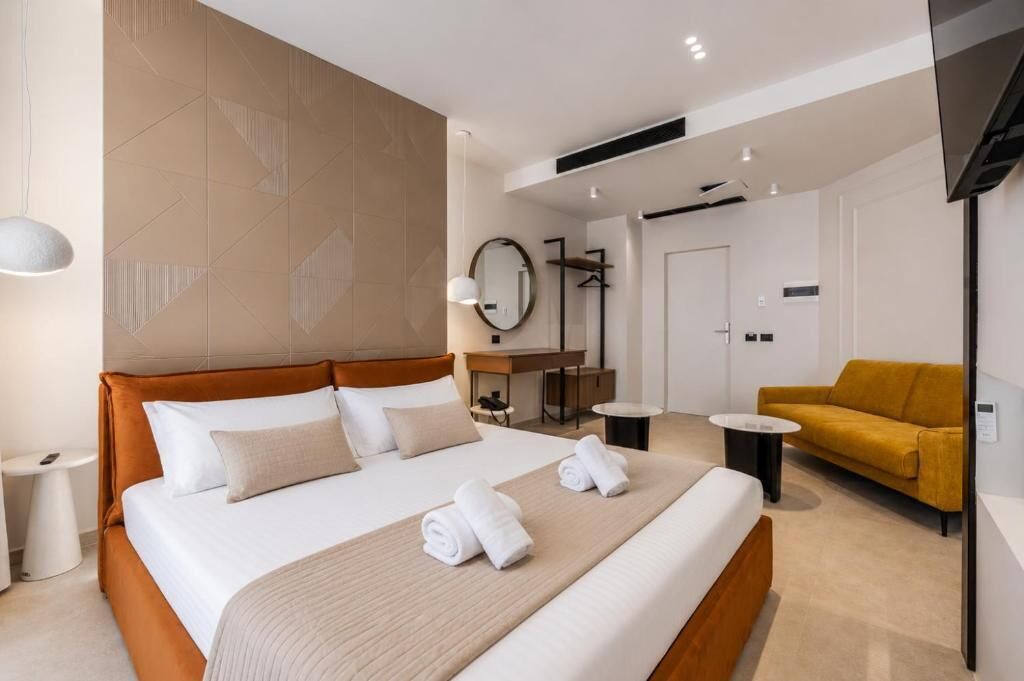 A modern hotel room with a large bed, a sofa, a desk, and a TV.