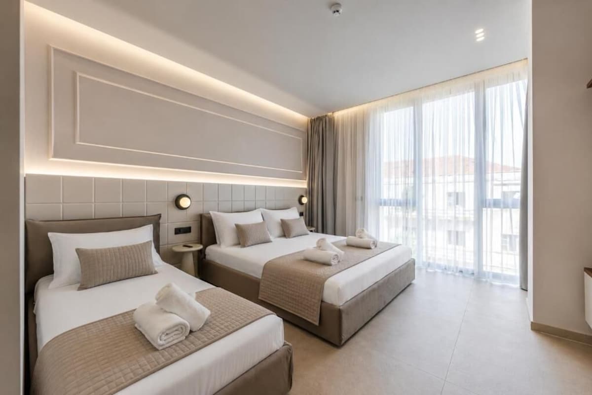 Ein Hotelzimmer mit zwei Betten, einem großen Fenster mit Vorhängen und einem modernen Deckenstil.