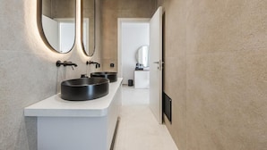 Un baño moderno con un espejo grande, dos lavamanos y una puerta que da a otra habitación.