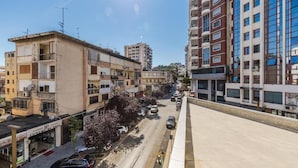 Un edificio de varios pisos con balcones, una calle con coches aparcados y cielo despejado.