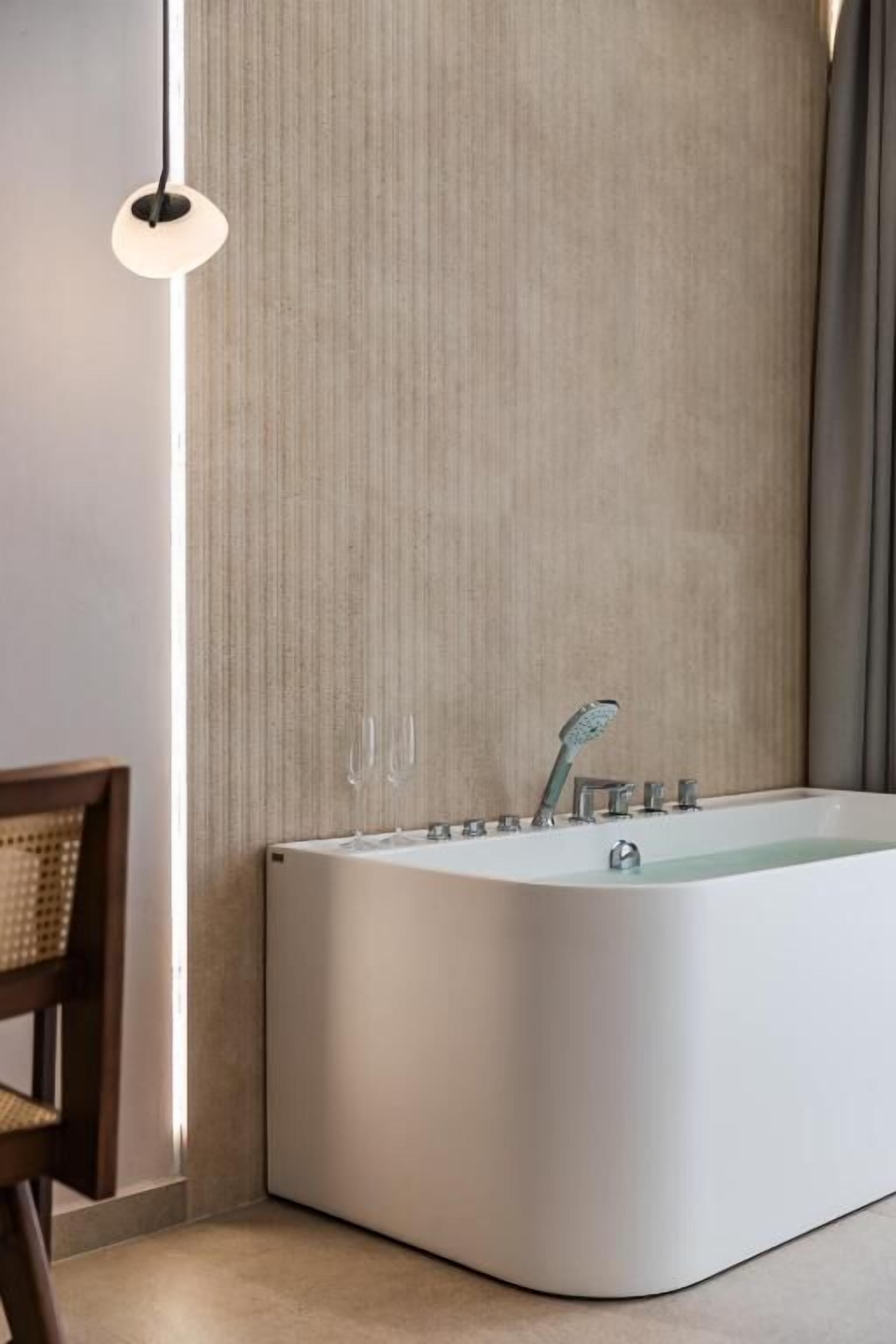 A modern bathroom with a freestanding bathtub, a wooden chair, and a hanging light fixture.
