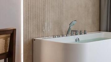 A modern bathroom with a freestanding bathtub, a wooden chair, and a hanging light fixture.