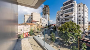 Vista desde un balcón sobre un paisaje urbano con edificios modernos, cielo despejado y una calle con coches estacionados.