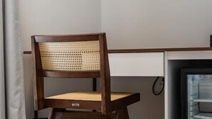 Una silla de madera con respaldo y asiento tejido, ubicada frente a un escritorio blanco con un televisor montado en la parte superior.