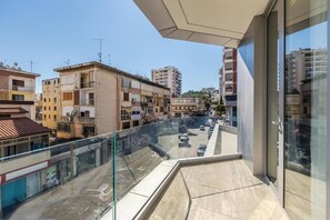 A balcony with a glass railing overlooking a street with parked cars and buildings.