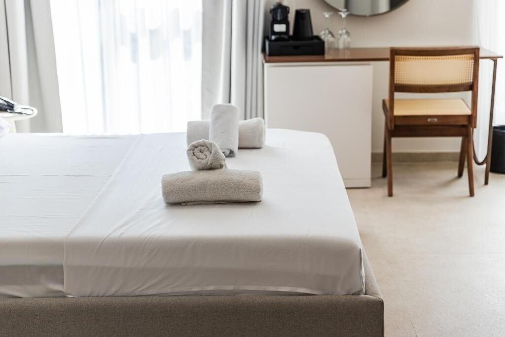 Habitación de hotel con una cama bien hecha, una silla de madera y un escritorio con cafetera.